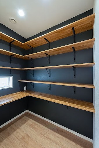 A contemporary walk in closet with bold black walls, wooden shelves, and unique bracket design for an open storage concept.
