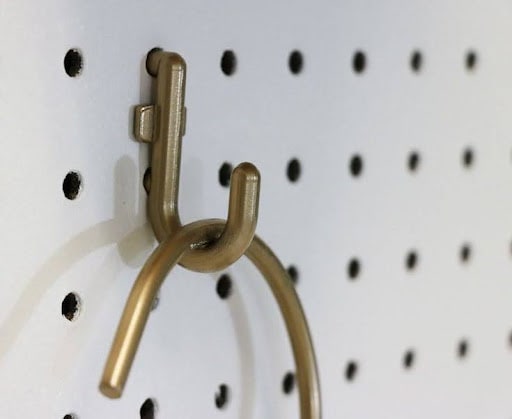 A close-up of a brass hook on a pegboard, exemplifying minimalist and functional design in a small walk in closet