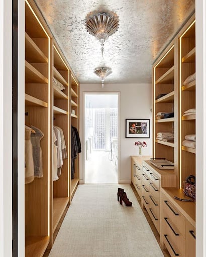 An elegant narrow walk-in closet with luxurious light fixtures and wood accents.
