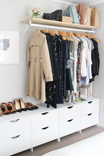 A small open closet with a high shelf for bags, a hanging rod, and spacious white drawers beneath.
