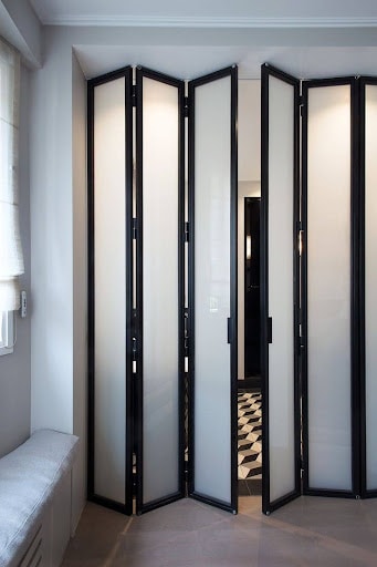  A set of modern black-framed Use of Accordion mirrored doors opening to a sleek wardrobe in a well-lit room.
