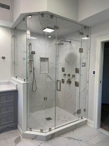 A Frameless Glass Enclosure corner shower in this small bathroom showcases marble-look tiles that create a luxurious atmosphere, enhanced by the sophisticated grey vanity unit beside it.
