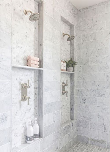 Luxuriously appointed small bathroom shower niche with marble tiling and a variety of showerheads, exuding sophistication in a compact form.