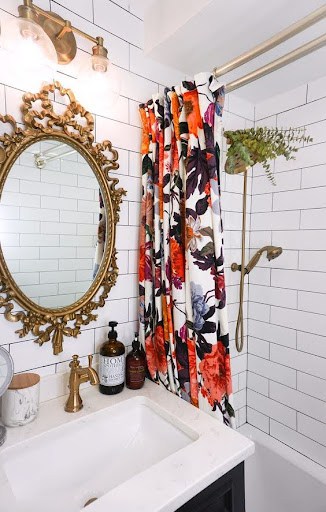 This small bathroom shower captures a bohemian vibe with its vibrant floral curtain, classic white subway tiles, antique gold mirror, and vintage-inspired brass fixtures.