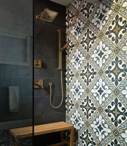 Tile Patterns and Colors in a small bathroom shower featuring bold patterned tiles and brass fixtures, with a wooden bench for convenience.
